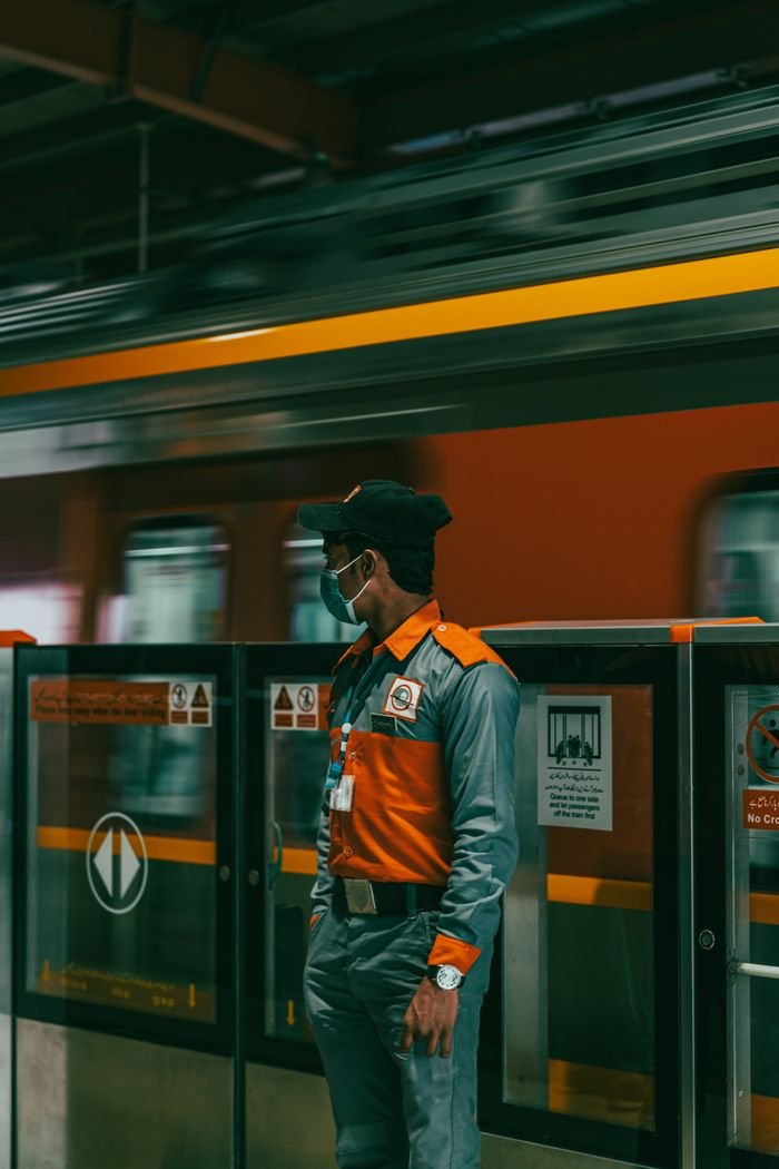 Security guard in uniform at Lahore metro station with a moving train in the background.