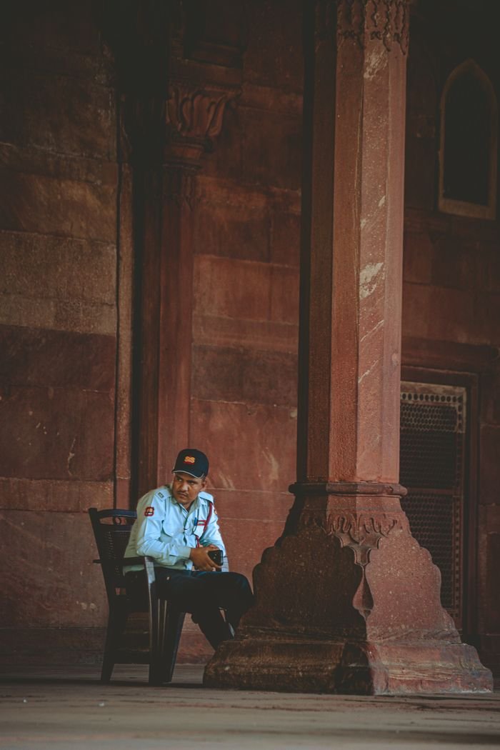A security guard seated by a large column in a historic building, reflecting on his duties.